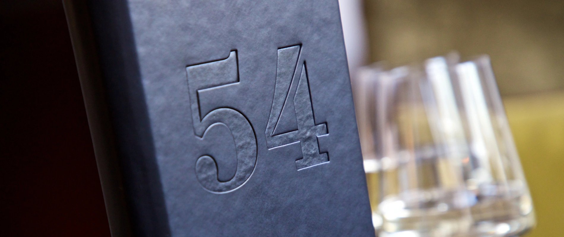 Embossed number "54" on a dark surface, blurred background.