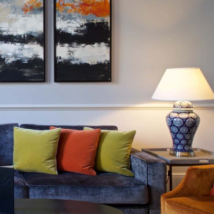 Living room with colorful cushions, abstract art, and a patterned lamp.