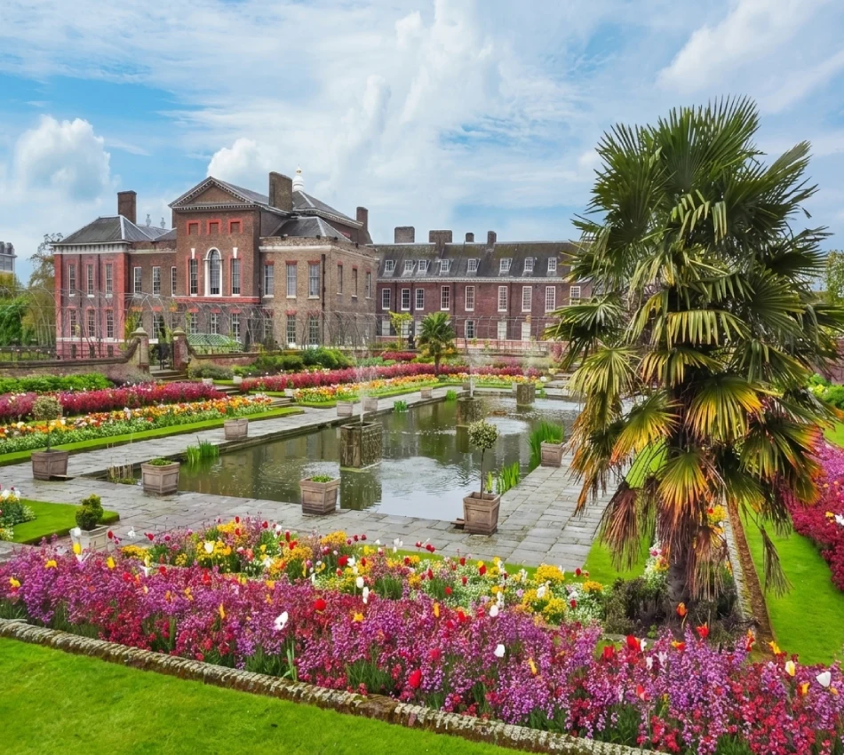 Garden with a pond and colorful flowers in front of a historic brick building.