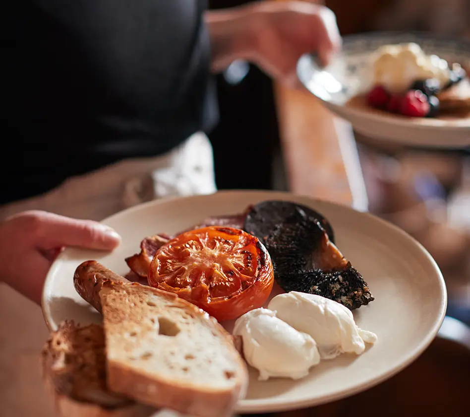 Plate with toast, poached eggs, tomato, black pudding, and bacon.