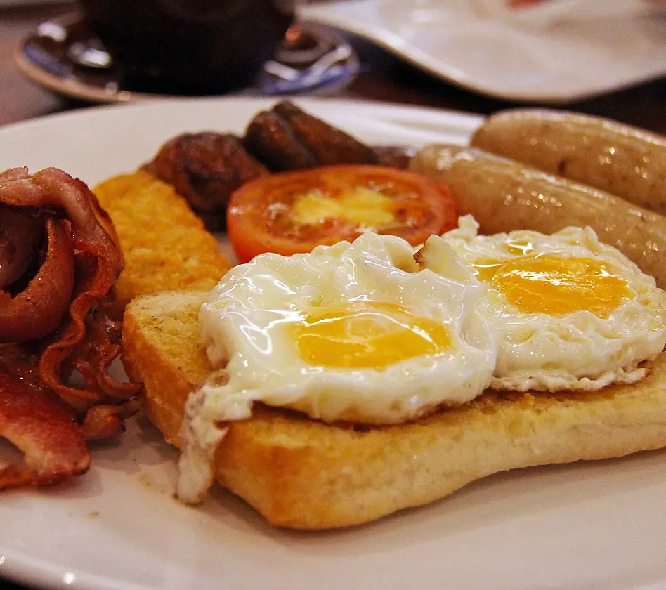 A plate with eggs, toast, bacon, sausages, tomato, and hash brown.
