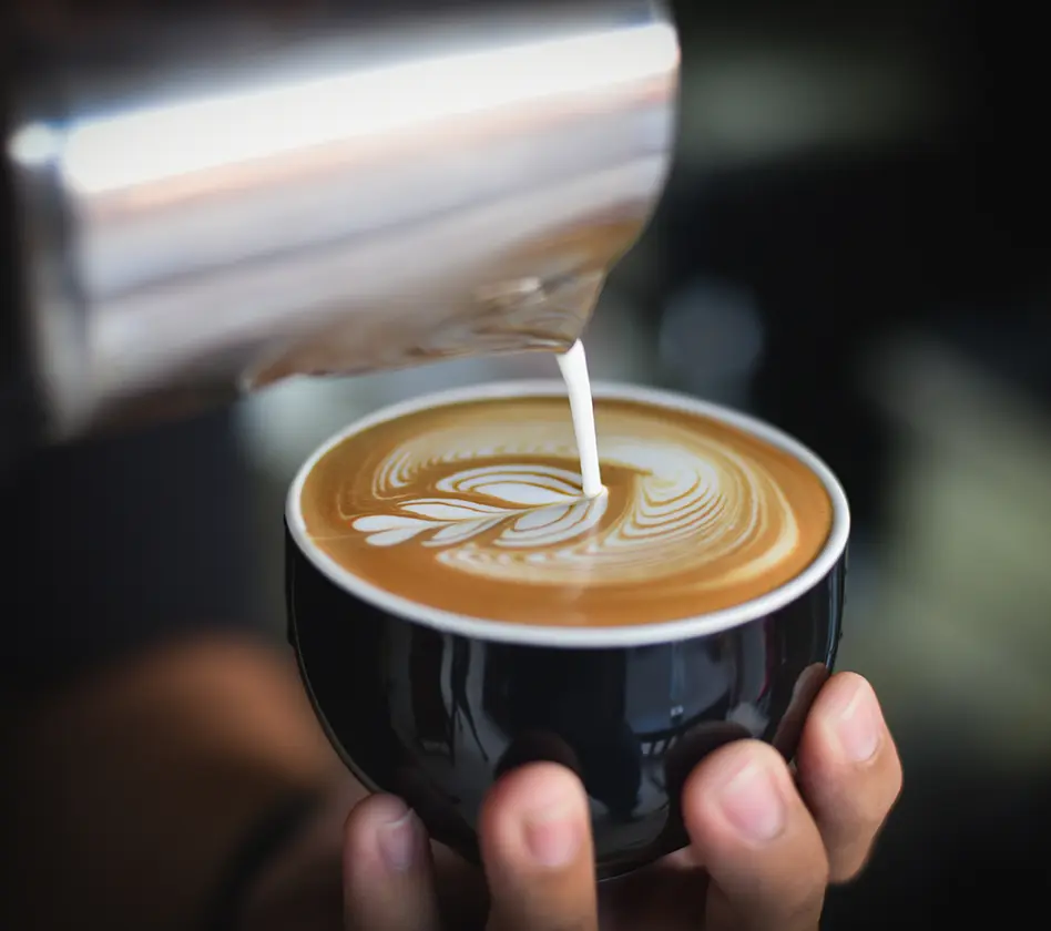 Pouring latte art into a black cup, forming a leaf pattern.