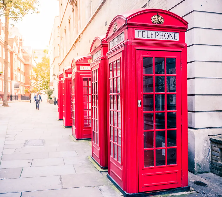 Red phone booths line a street in a sunny urban setting.