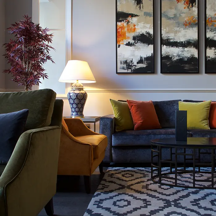 Stylish living room with colorful pillows, artwork, and a table lamp.