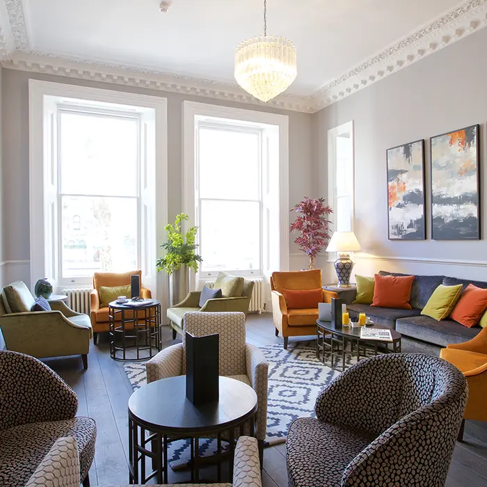 A modern living room with colorful chairs, a sofa, plants, and large windows.