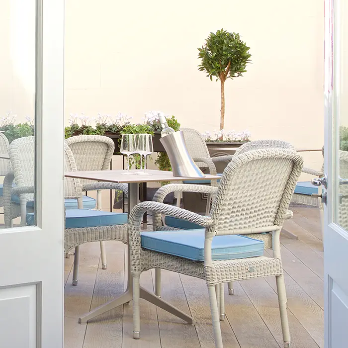 Outdoor patio with wicker chairs, blue cushions, and a tree.