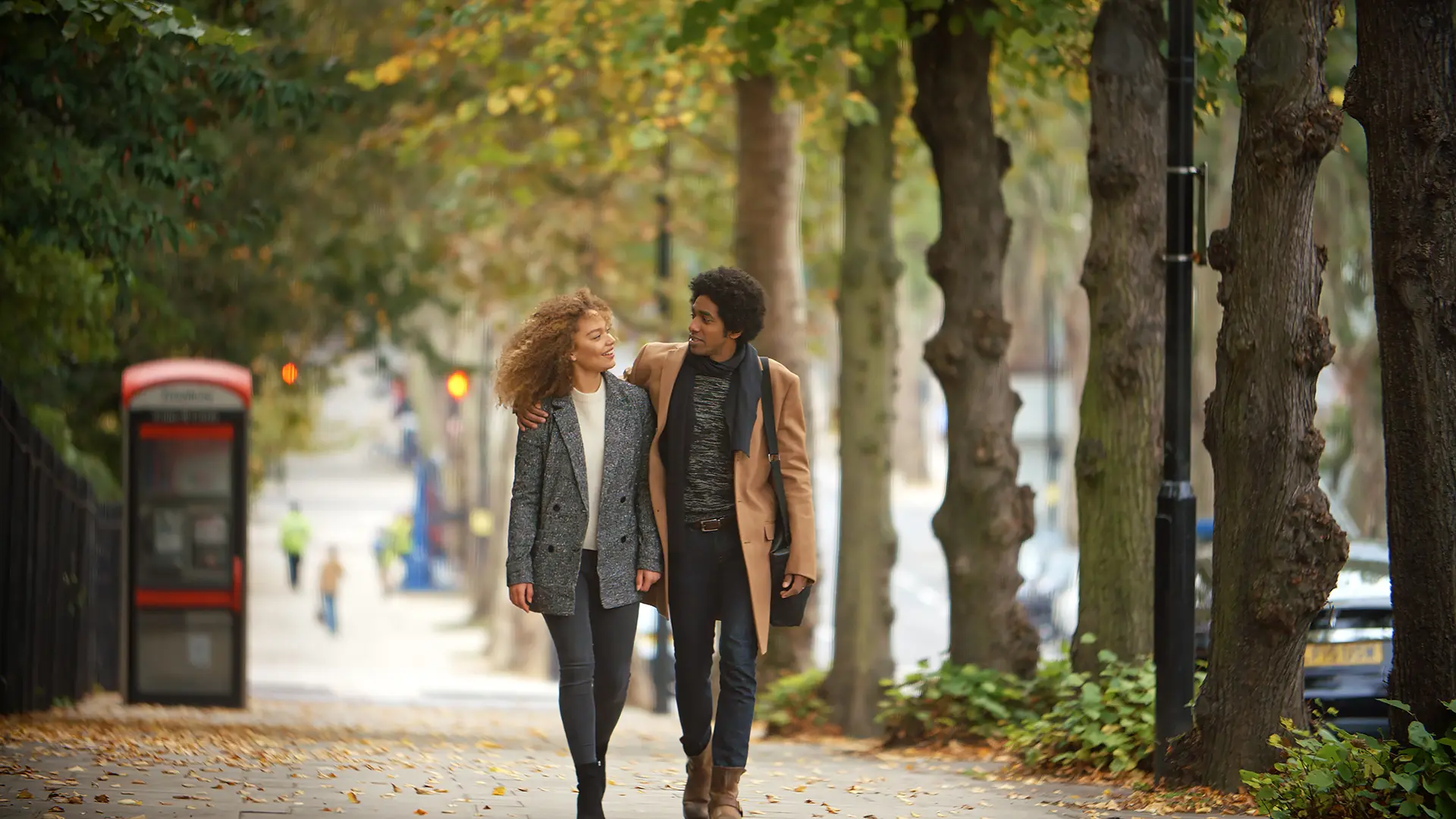 Couple walking arm in arm on a tree-lined sidewalk.