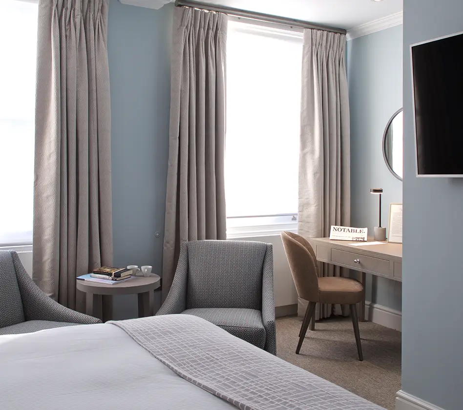 Cozy hotel room with two chairs, a bed, and a desk by the window.