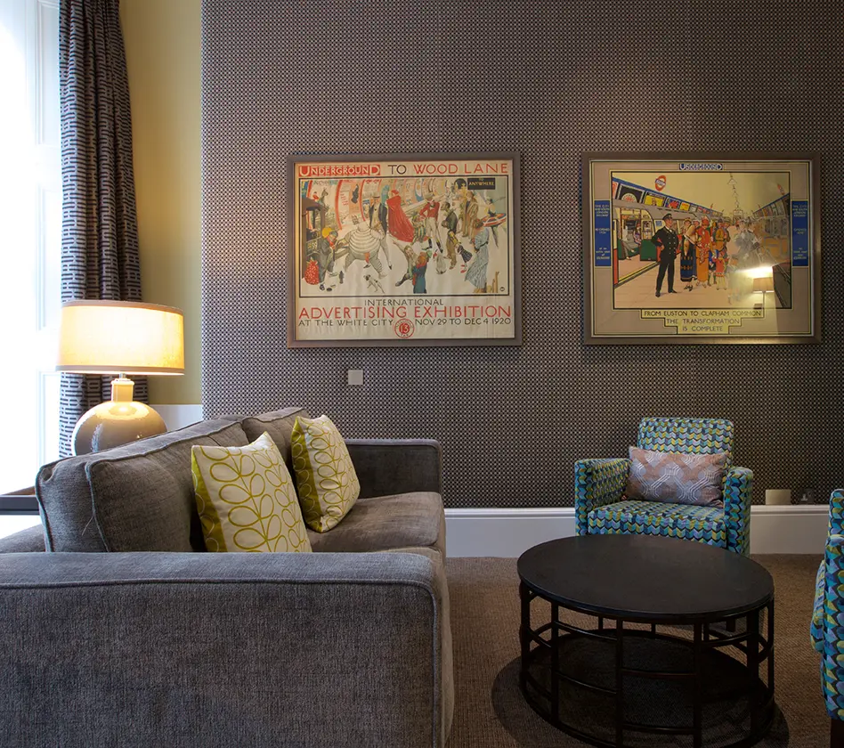 Cozy living room with a gray sofa, patterned chairs, and vintage posters.