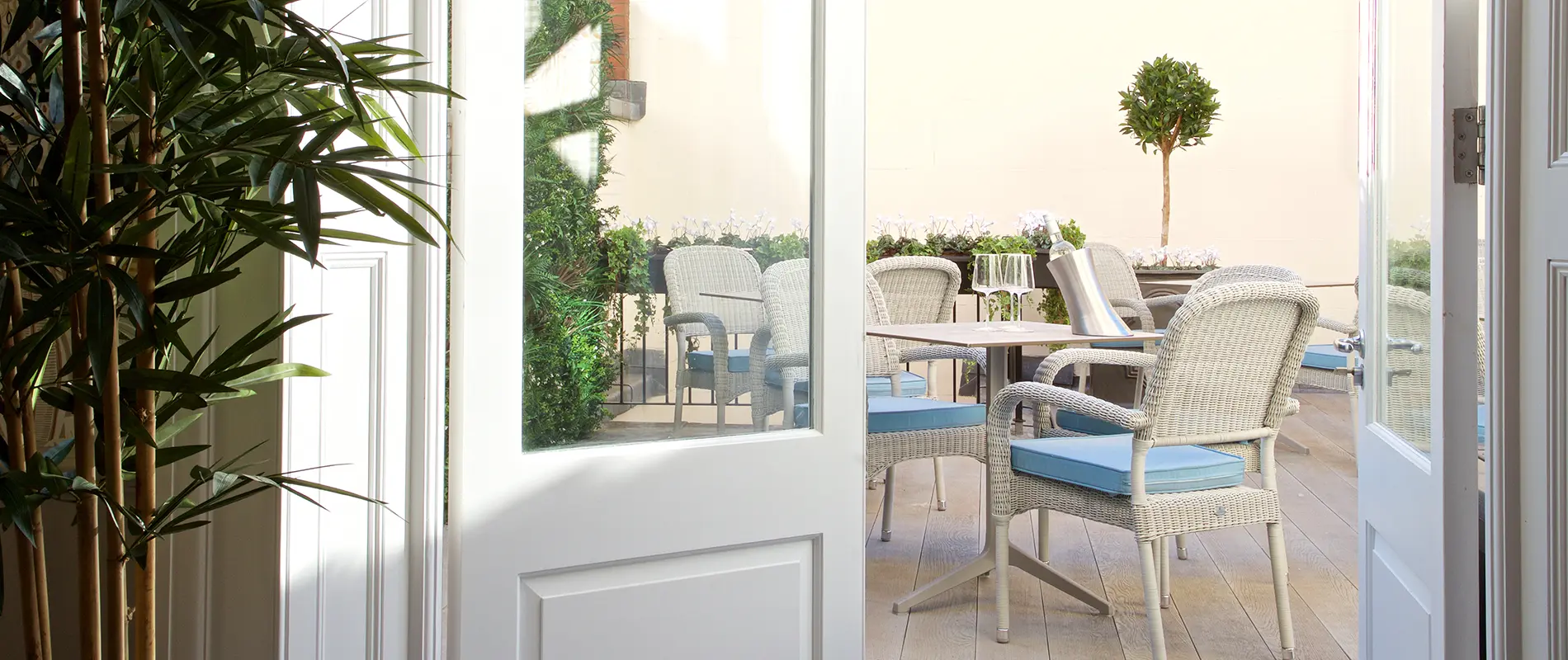 Wicker chairs and table on a sunny patio, seen through open door.