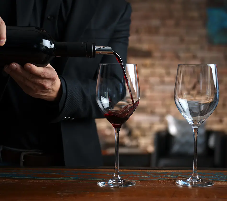 Person pouring red wine into a glass on a wooden table.