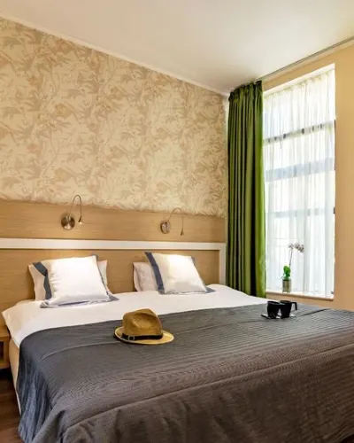 Cozy bedroom with double bed, hat, and coffee cups near a window.