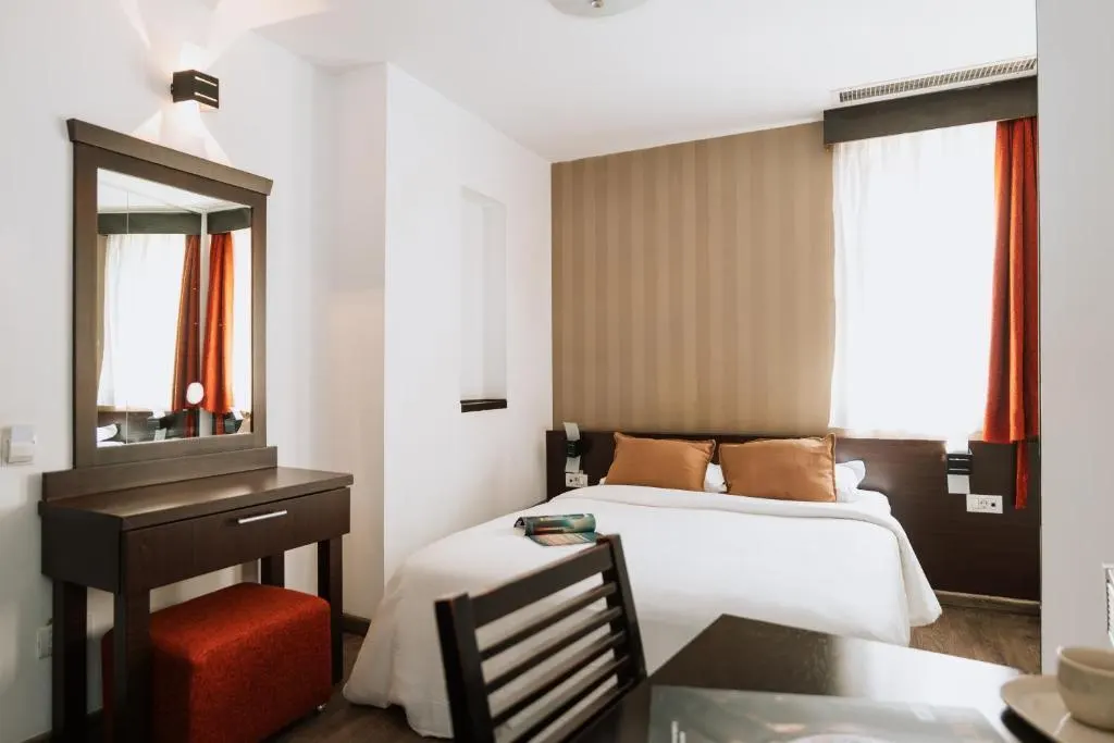 Hotel room with bed, desk, mirror, and red curtains.