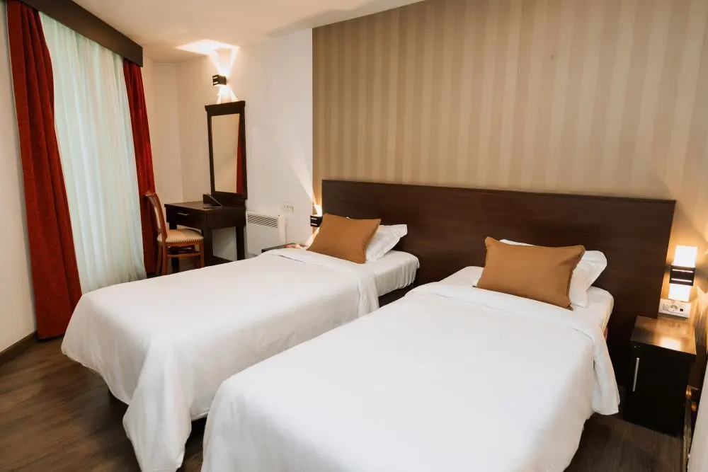 Minimalist hotel room with two beds, a desk, and warm lighting.