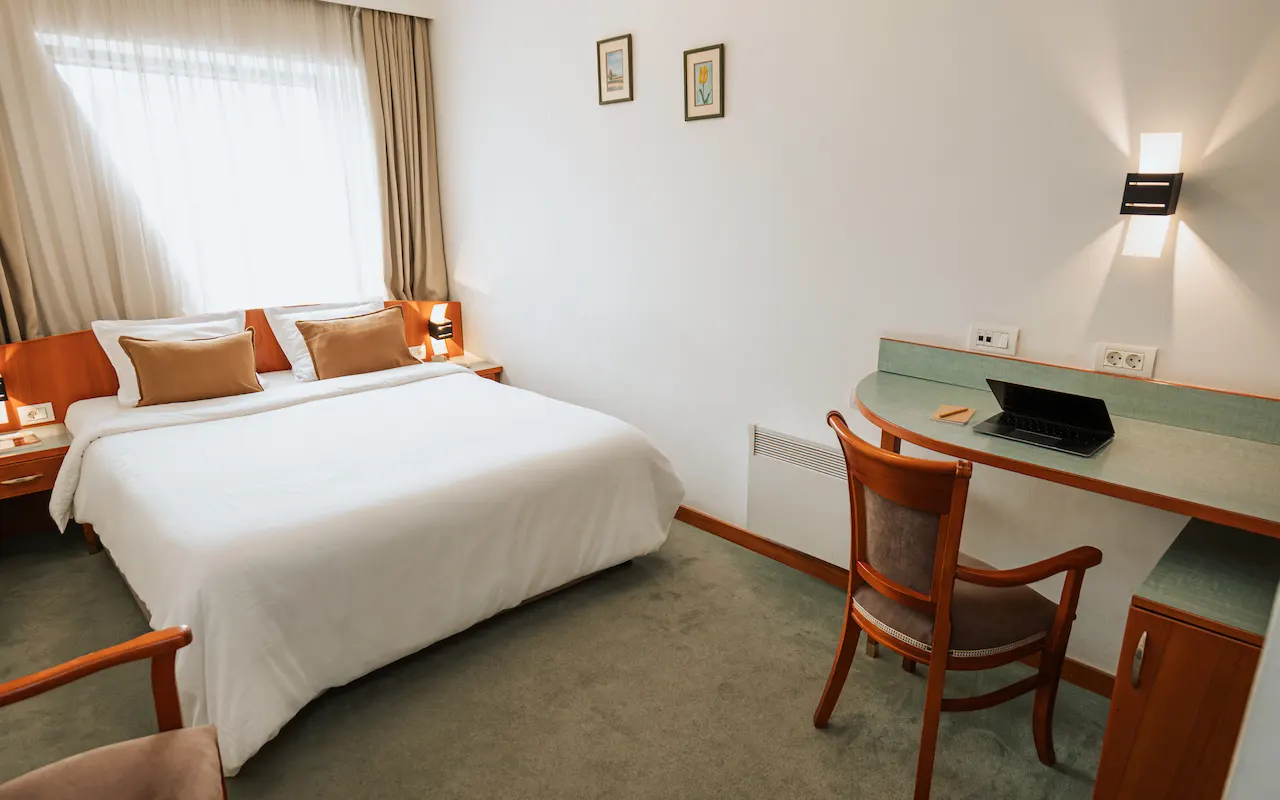 Hotel room with a bed, desk, chair, and a laptop on the table.