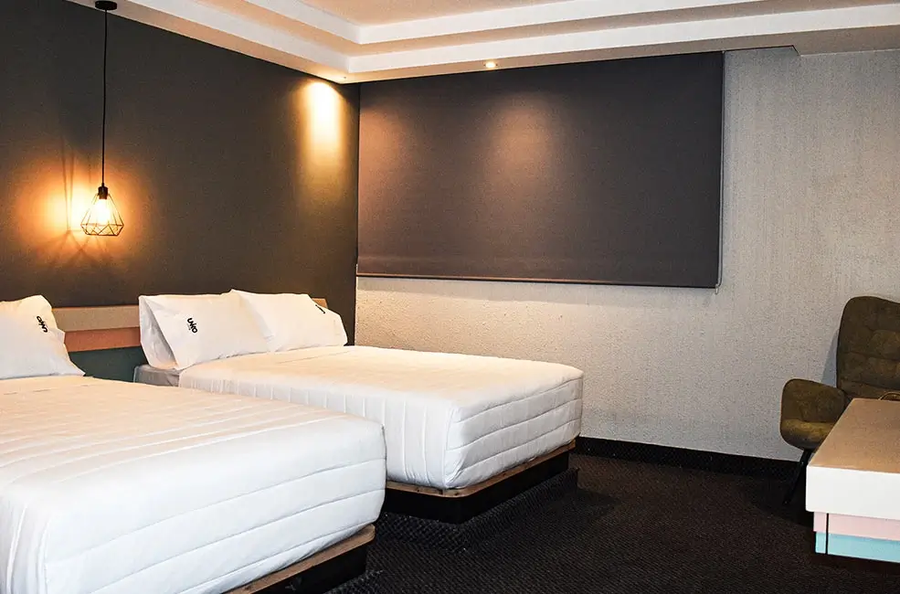 Habitaci&oacute;n de hotel con dos camas, luz tenue y dise&ntilde;o moderno.