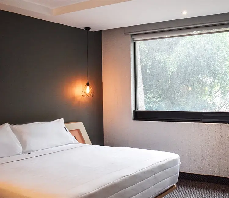 Habitaci&oacute;n moderna con cama, l&aacute;mpara colgante y ventana grande.