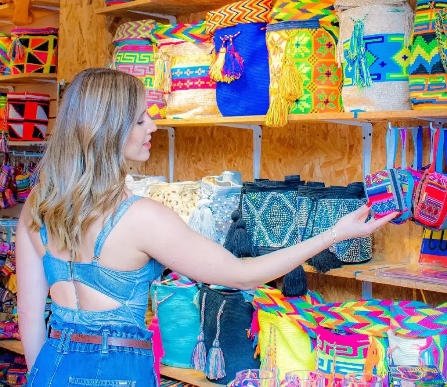 Mujer observando bolsos coloridos y tejidos en una tienda de artesan&iacute;as.