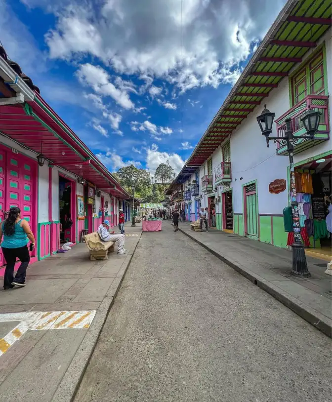 Calle colorida con edificios coloniales y personas paseando bajo un cielo azul y nubes.