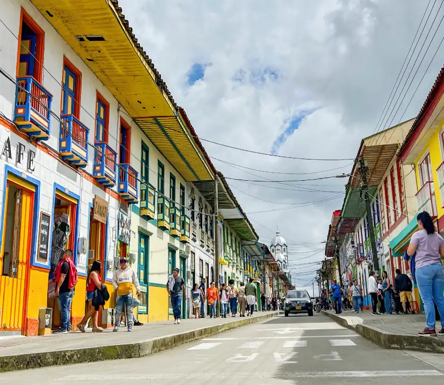 Calle con casas coloridas y personas paseando; cielo nublado en el fondo.