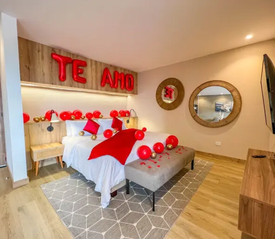 Habitaci&oacute;n decorada con globos rojos y dorados y la frase "Te amo" sobre la cama.