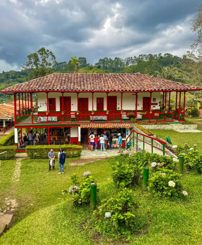 Casa campestre colorida rodeada de c&eacute;sped y visitantes bajo un cielo nublado.