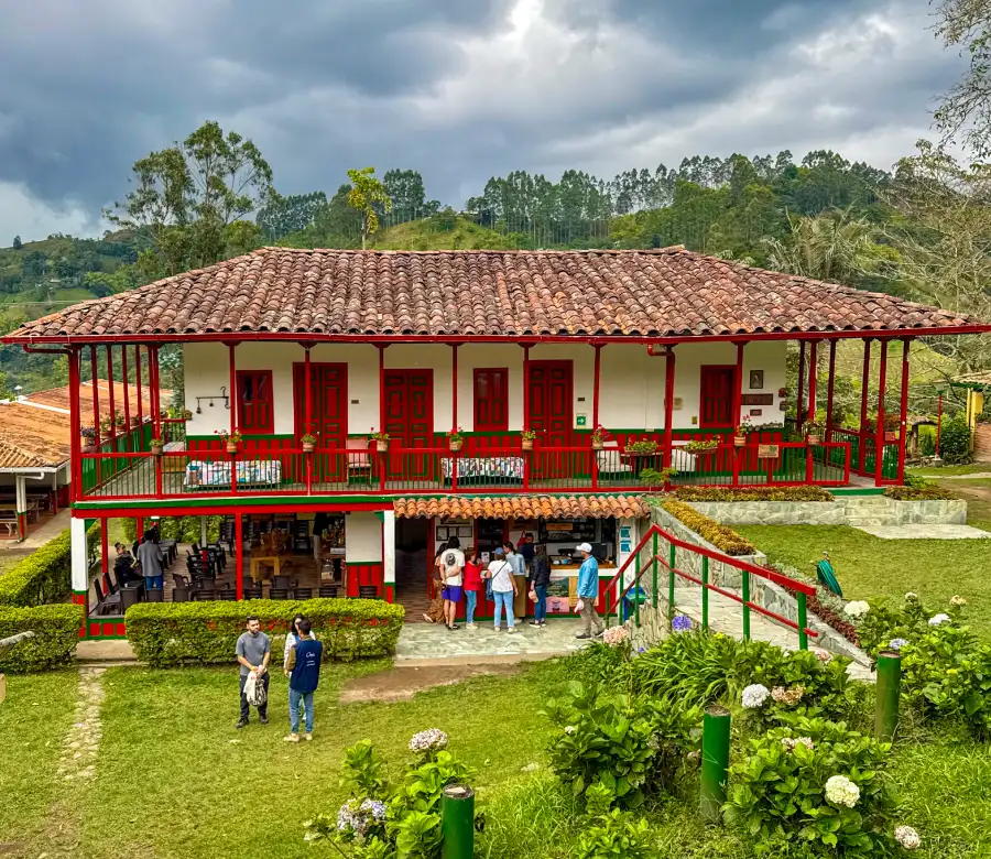 Casa tradicional con balcones rojos y techo de tejas rodeada de naturaleza y personas.