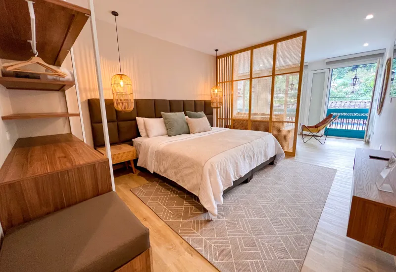 Dormitorio moderno con cama grande, alfombra geom&eacute;trica y vista al exterior.