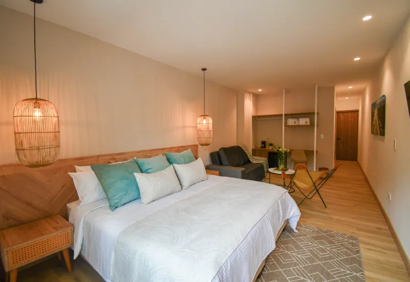 Habitaci&oacute;n moderna con cama, sof&aacute;, l&aacute;mparas colgantes y detalles de madera.