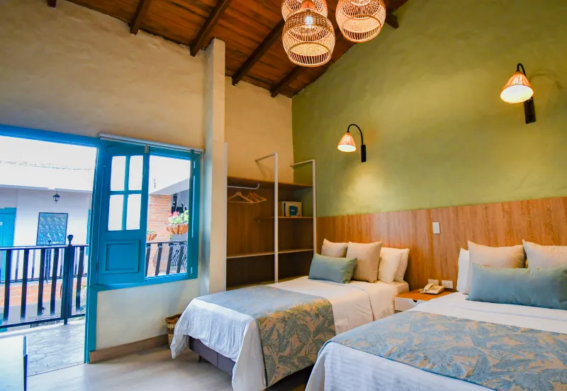 Habitaci&oacute;n acogedora con dos camas, decoraci&oacute;n r&uacute;stica y puerta azul abierta a un balc&oacute;n.