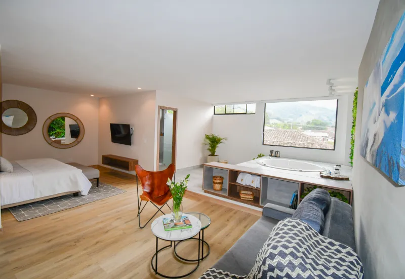 Habitaci&oacute;n moderna con cama, sof&aacute;, mesa, ba&ntilde;era y gran ventana. Decoraci&oacute;n elegante y luminosa.