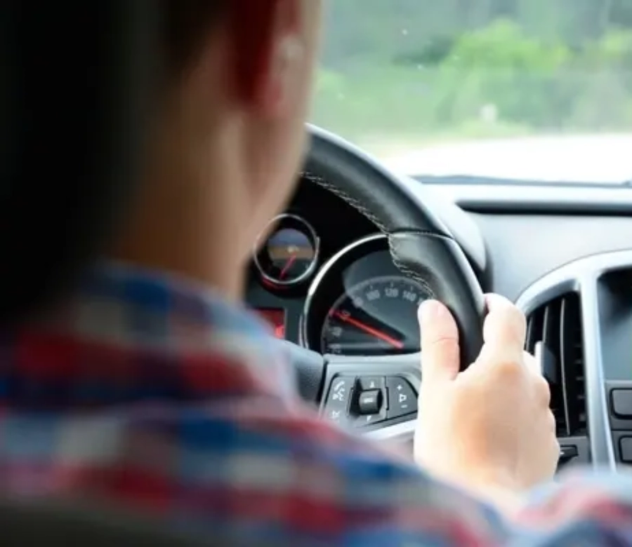 Persona conduciendo un autom&oacute;vil, vista desde atr&aacute;s. Volante y tablero del coche visibles.
