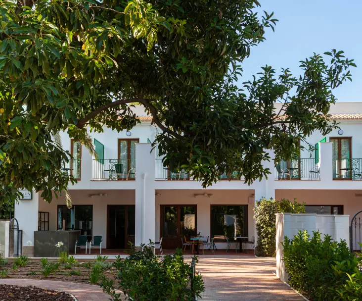 Fachada de una casa blanca con &aacute;rboles y jard&iacute;n al frente, cielo despejado.