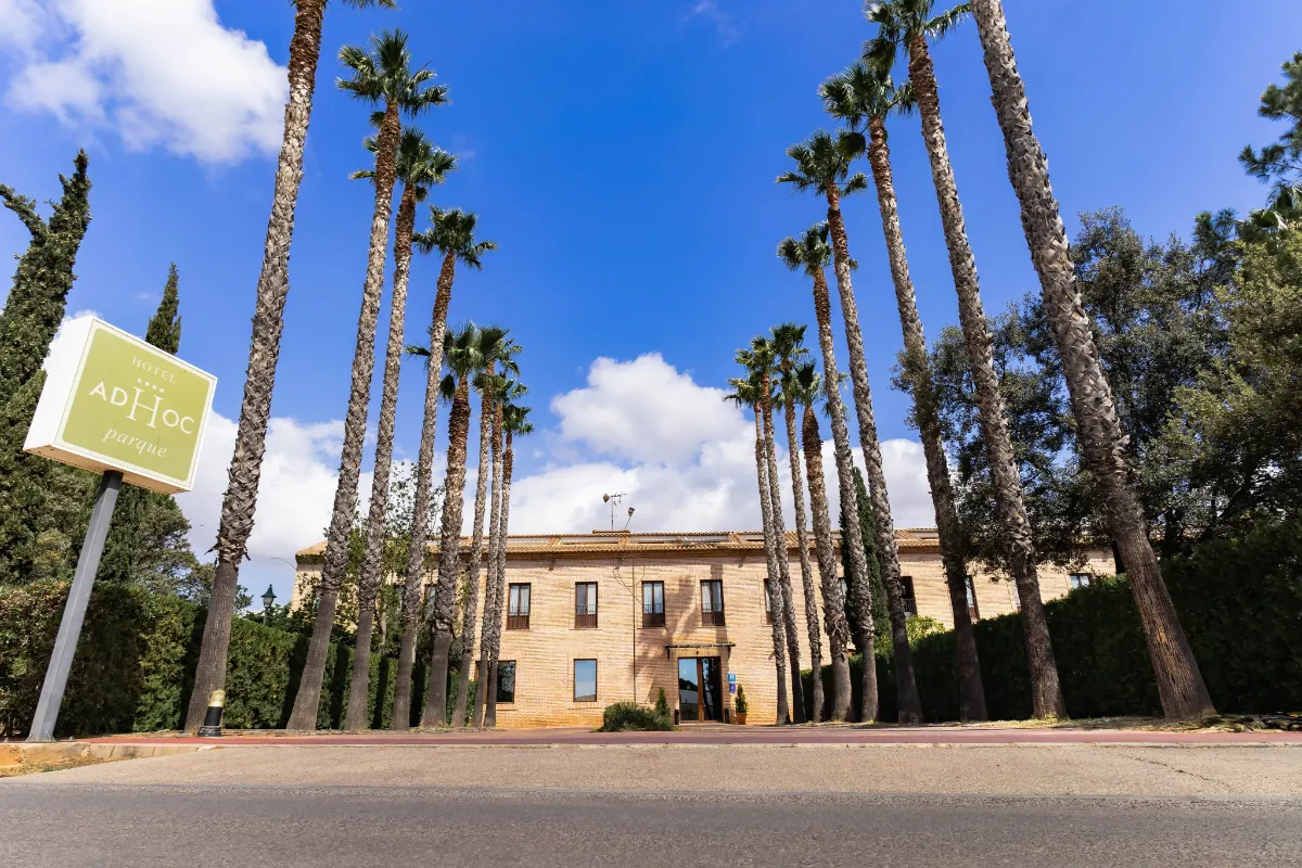 Fachada de un hotel con palmeras altas y cielo azul despejado.
