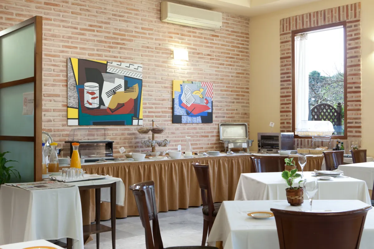 Restaurante acogedor con mesas vestidas y buffet variado; obras de arte coloridas decoran la pared.