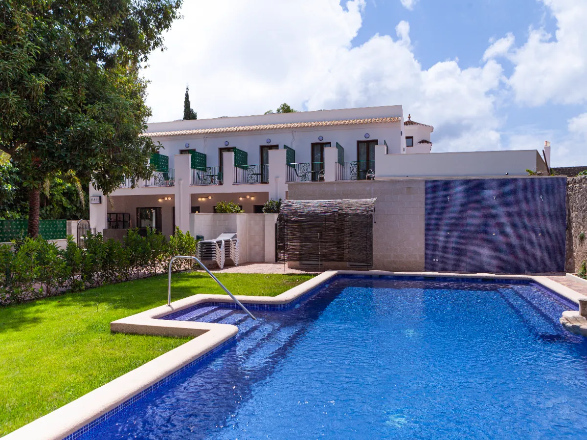 Casa blanca de dos pisos con piscina y jard&iacute;n verde, cielo azul con nubes.
