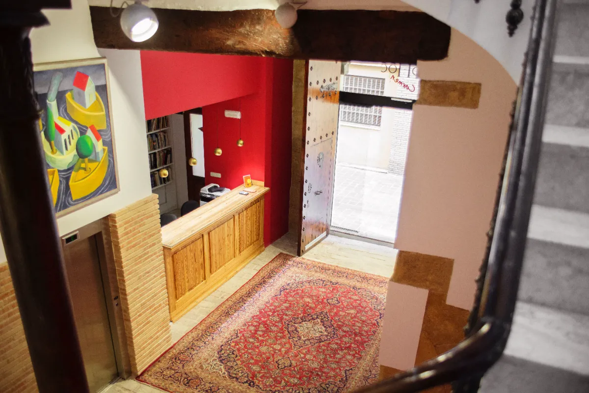 Hall de entrada con alfombra roja, mostrador de madera, puerta abierta y cuadro colorido en la pared.