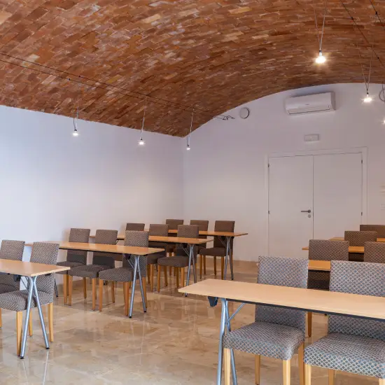Aula con techo de ladrillo abovedado, sillas y mesas dispuestas en filas.