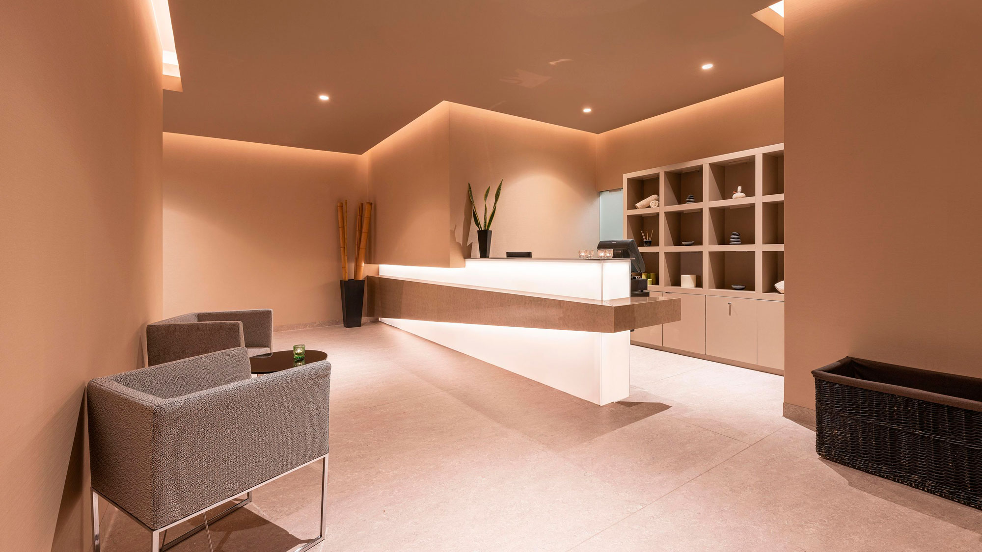 Modern reception area with chairs, desk, and shelves in warm lighting.