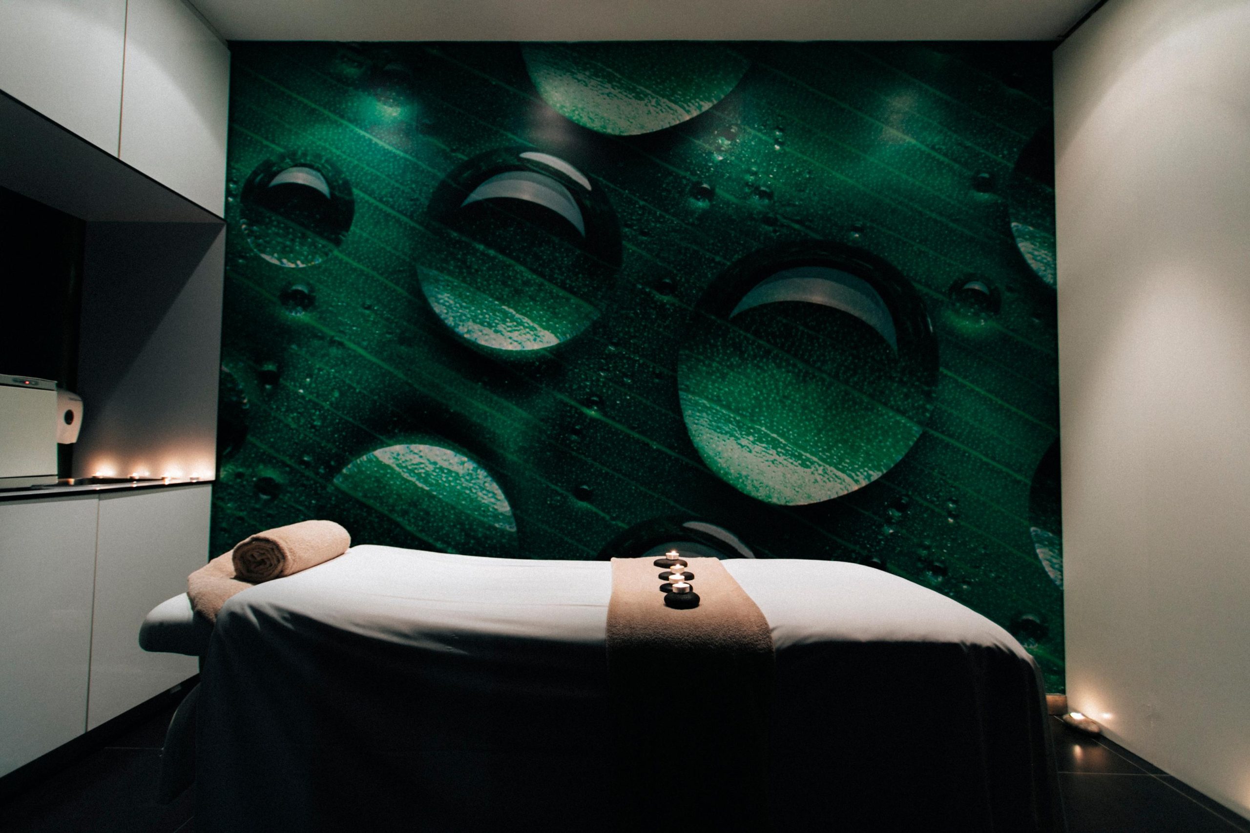 Massage table in a dim room with a green wall featuring water droplets.