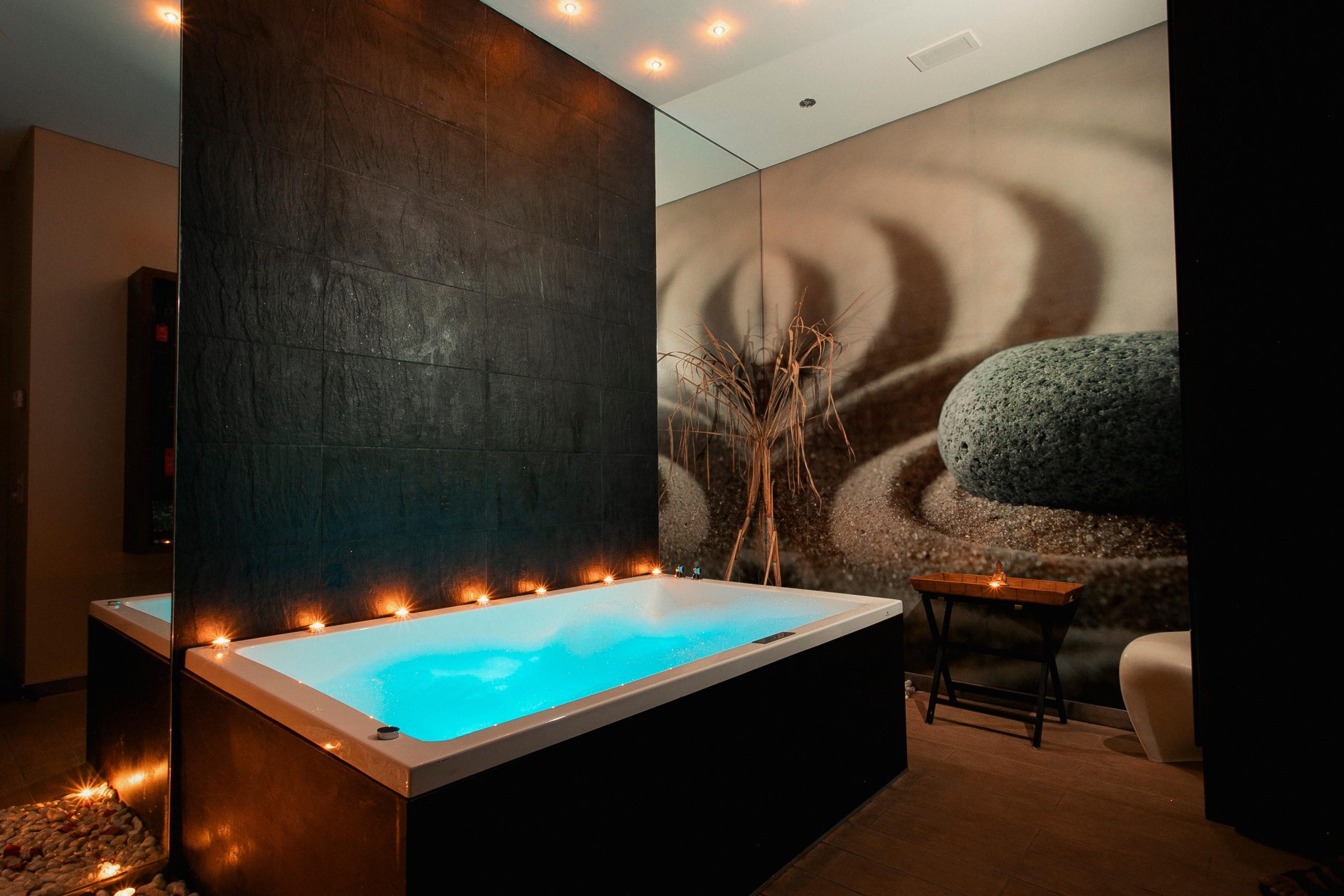 Lit Jacuzzi in a dim spa room with candles against a stone-patterned wall.