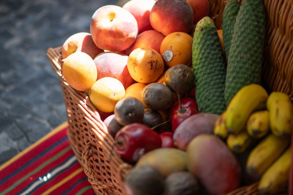 A basket of assorted fruits in sunlight on a colorful cloth.