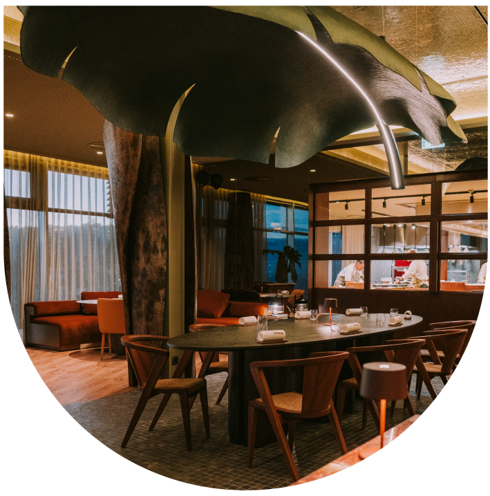 Cozy restaurant interior with a large leaf decor and chefs visible in the kitchen.