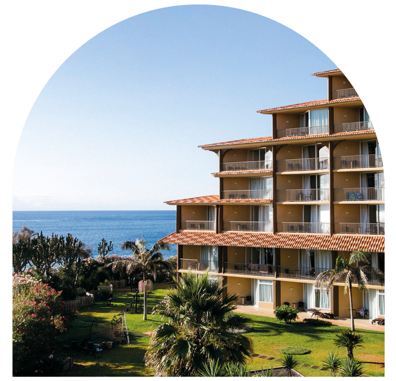 Seaside hotel with palm trees and ocean view under a clear blue sky.