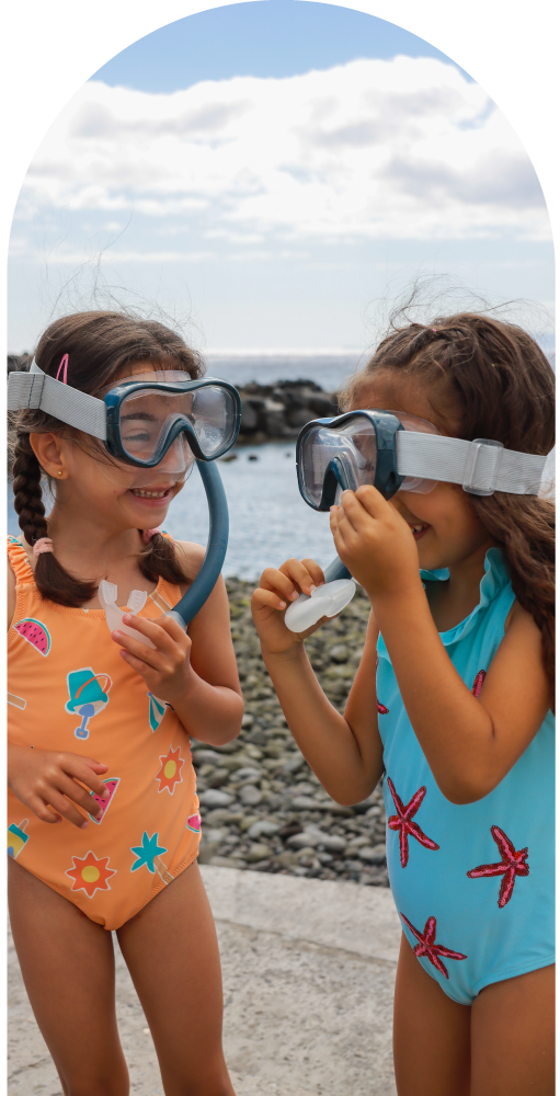 Two kids in swimsuits smiling with snorkeling gear by the beach.