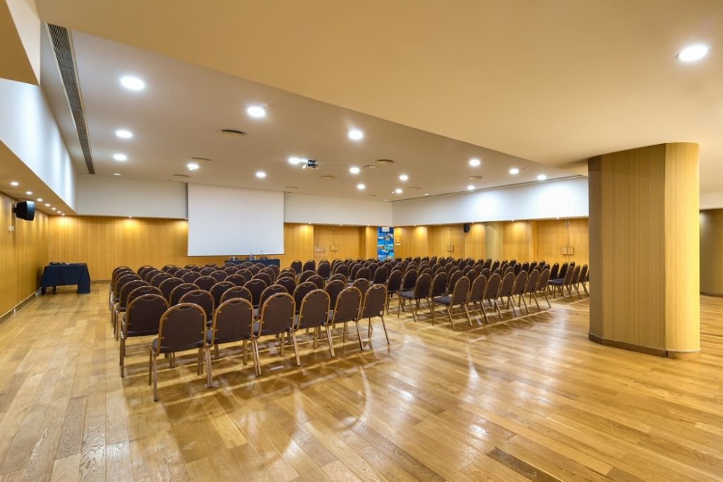 An empty conference room with rows of chairs and a projection screen.