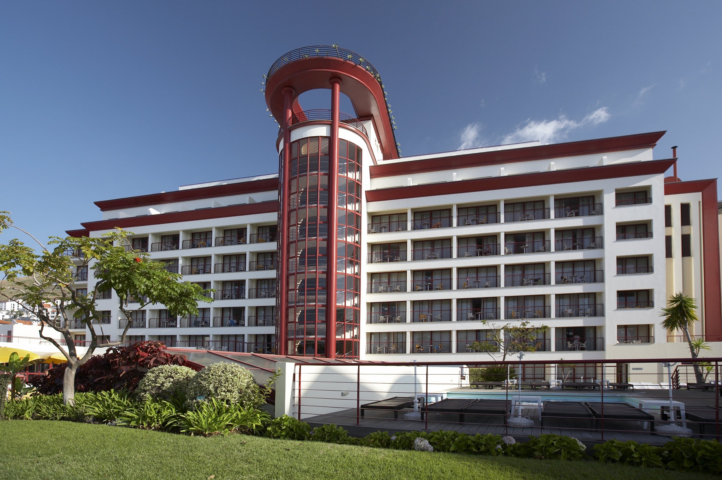 Modern building with red accents, blue sky, and surrounding greenery.