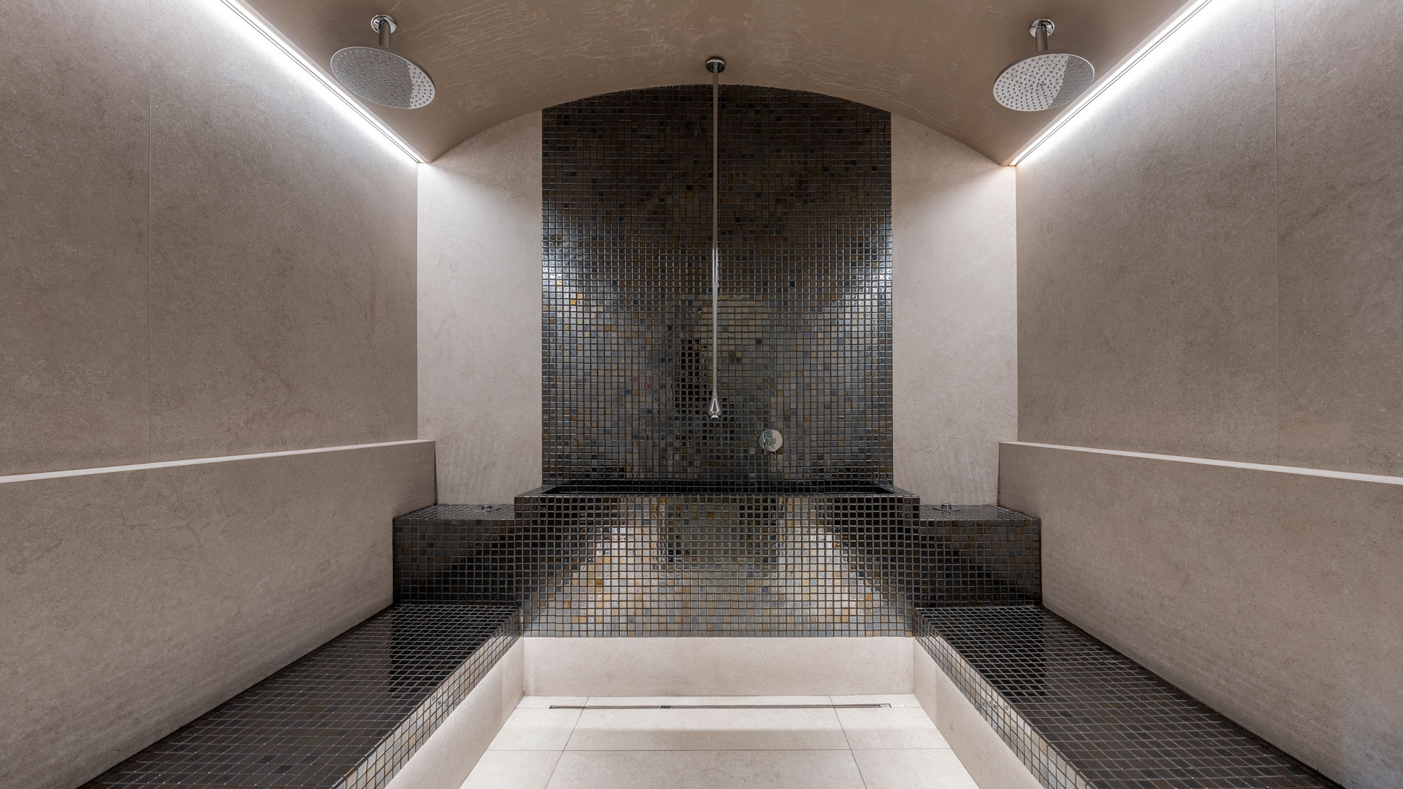 Modern steam room with mosaic tiles and two overhead shower heads.