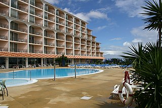 Hotel with balconies overlooking a large pool and palm.