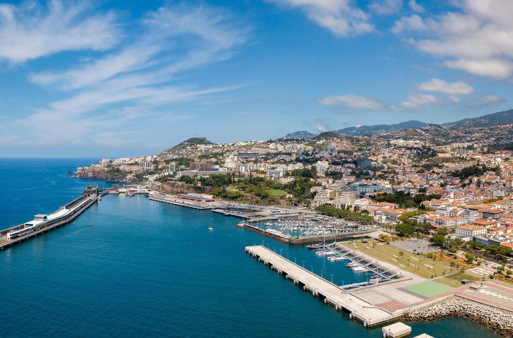 Aerial view of a coastal city with a harbor and mountains under a clear blue sky.